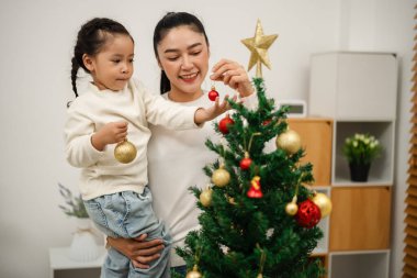 Mutlu anne ve küçük kız Noel ağacını evde oyuncak topla süslüyorlar.
