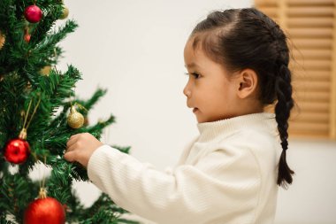 Mutlu küçük kız evde Noel ağacını süslüyor.