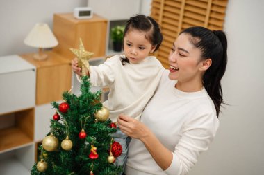 Mutlu anne ve küçük kız evdeki Noel ağacında süsleme yapıyor.