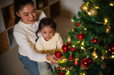 Mutlu anne ve küçük kız gece evde Noel ağacı süslüyorlar.
