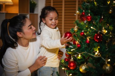 Mutlu anne ve küçük kız gece evde Noel ağacı süslüyorlar.