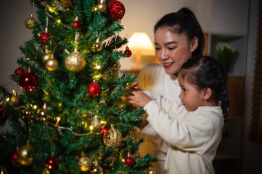 Mutlu anne ve küçük kız gece evde Noel ağacı süslüyorlar.