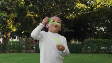 Parkta sabun köpüğü üfleyerek yürüyen mutlu kızın ağır çekimleri.