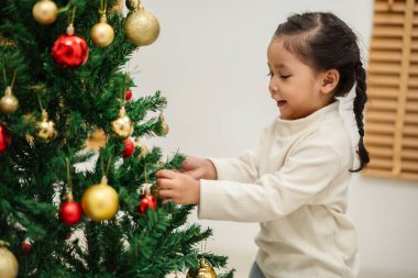 Mutlu küçük kız evde Noel ağacını süslüyor.