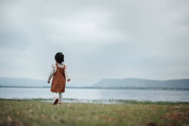 Nehrin kenarındaki çim tarlasında yürüyen mutlu küçük kız.