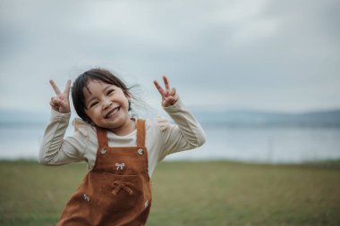 Nehrin kenarındaki çim tarlasında barış işareti yapan küçük mutlu bir kız.