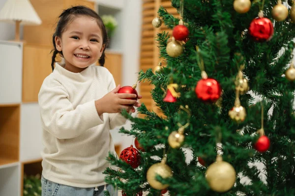 Mutlu küçük kız evde Noel ağacında oyuncak balosu düzenliyor.