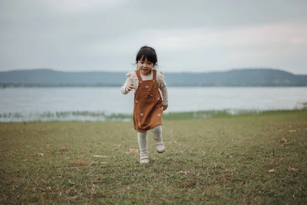 Nehrin kenarındaki çim tarlasında koşan mutlu kız.