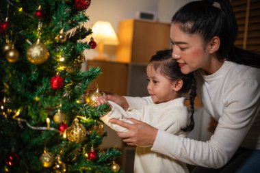 Mutlu anne ve küçük kız gece evde Noel ağacı süslüyorlar.