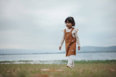 Nehrin kenarındaki çim tarlasında yürüyen mutlu küçük kız.