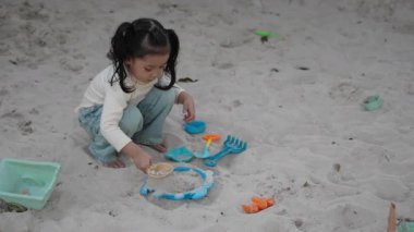 Çocuk parkında oyuncakla kum oynayan mutlu kızın yavaş çekimleri.