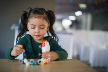 Çocuk kız masaya alçı heykel boyuyor.