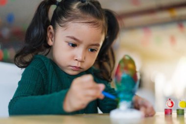 Çocuk kız masaya alçı heykel boyuyor.