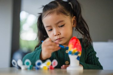 Çocuk kız masaya alçı heykel boyuyor.