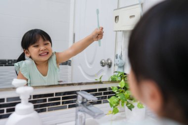 Banyoda aynadaki yansımada dişlerini fırçalayan bir kız çocuğu.