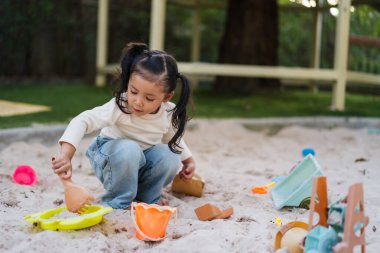 Çocuk bahçesinde oyuncakla kum oynayan mutlu bir kız çocuğu.