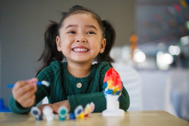Çocuk kız masaya alçı heykel boyuyor.