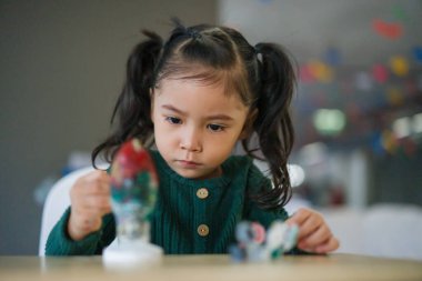 Çocuk kız masaya alçı heykel boyuyor.