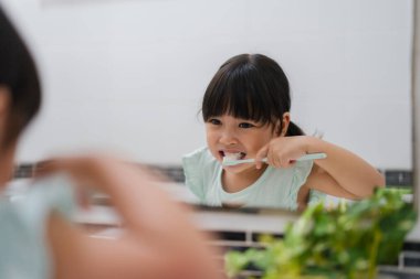 Banyoda aynadaki yansımada dişlerini fırçalayan bir kız çocuğu.