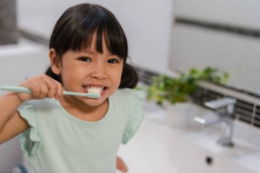 Kız çocuk banyoda dişlerini fırçalıyor.