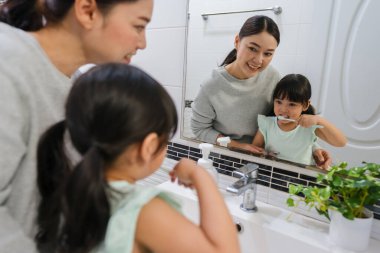 Anne, kız çocuğuna banyodaki aynada dişlerini fırçalamayı öğretiyor.