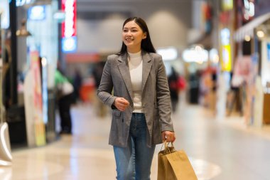 Bir alışveriş merkezinde alışveriş çantasıyla gezen mutlu bir anne.