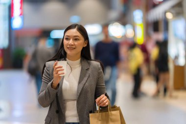 Alışveriş merkezinde alışveriş yaparken elinde bir fincan kahve ve poşet tutan bir kadın.