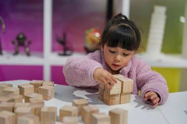 Anaokulundaki kız çocuğu ahşap bloklu bir kule inşa etmeye odaklanmış.