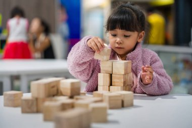 Anaokulundaki kız çocuğu ahşap bloklu bir kule inşa etmeye odaklanmış.