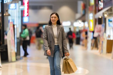 Bir alışveriş merkezinde alışveriş çantasıyla gezen mutlu bir anne.
