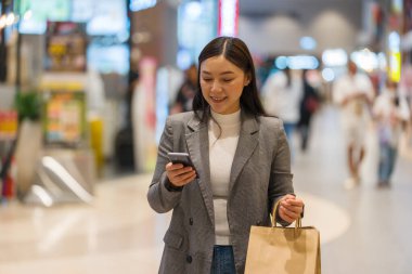 Alışveriş merkezinde alışveriş yaparken akıllı telefon kullanan bir kadın.