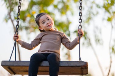 Neşeli kız çocuk parkta salıncakta oynuyor.