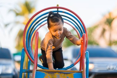 Çocuk, halka açık bir oyun parkındaki renkli metal tünel yapısında sürünüyor.