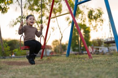 Neşeli kız çocuk parkta salıncakta oynuyor.