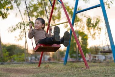 Neşeli kız çocuk parkta salıncakta oynuyor.
