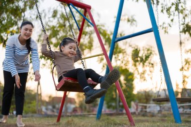 Neşeli kız ve annesi oyun parkında salıncakta oynuyorlar.