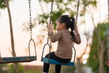 Neşeli kız çocuk parkta salıncakta oynuyor.
