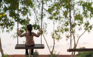 Neşeli kız çocuk parkta salıncakta oynuyor.