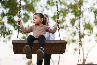 Neşeli kız ve annesi oyun parkında salıncakta oynuyorlar.
