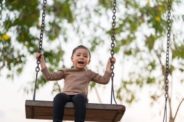 Neşeli kız çocuk parkta salıncakta oynuyor.