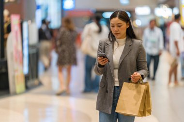 Alışveriş merkezinde alışveriş yaparken akıllı telefon kullanan bir kadın.