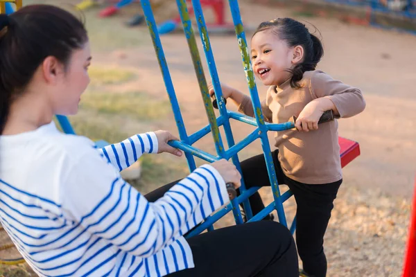 Neşeli çocuk annesi ile açık hava çocuk parkında çifte salıncakta oynuyor.