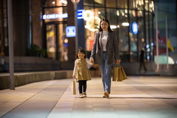 Anne ve küçük kız ellerinde alışveriş çantası ve gece Bangkok 'u geziyorlar.
