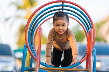 Çocuk, halka açık bir oyun parkındaki renkli metal tünel yapısında sürünüyor.