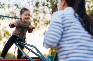 Neşeli kız ve anne açık alanda tahterevalli oynuyorlar.