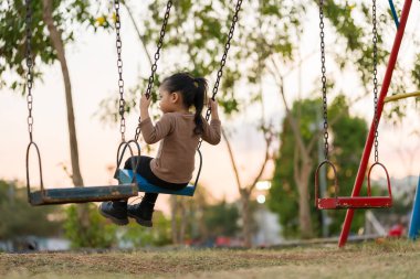 Neşeli kız çocuk parkta salıncakta oynuyor.