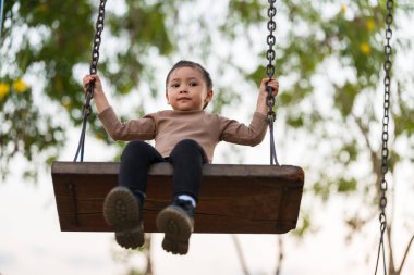 Neşeli kız çocuk parkta salıncakta oynuyor.