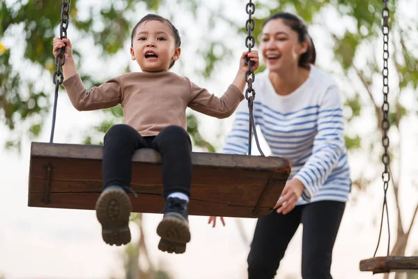 Neşeli kız ve annesi oyun parkında salıncakta oynuyorlar.
