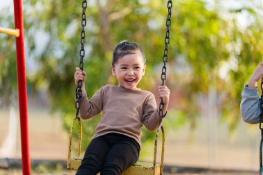 Neşeli kız çocuk parkta salıncakta oynuyor.