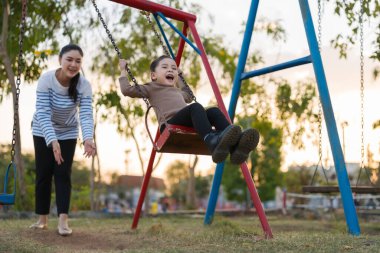 Neşeli kız ve annesi oyun parkında salıncakta oynuyorlar.